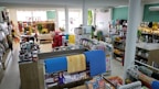 A well-organized store interior with neatly arranged products. Various home goods and decorations are displayed, including kitchenware, artificial flowers, and textiles. Shelves are filled with neatly stacked items, and the store is brightly lit with natural and artificial light.