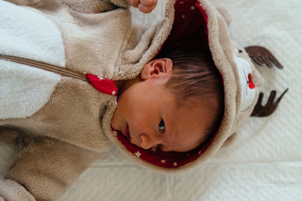 baby in white and red shirt lying on white textile