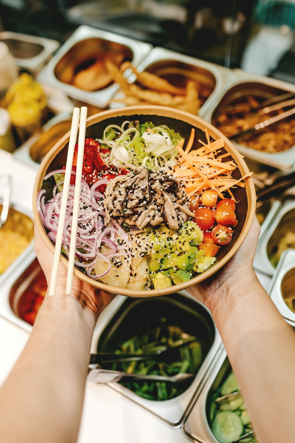 person holding brown wooden chopsticks with green vegetable salad