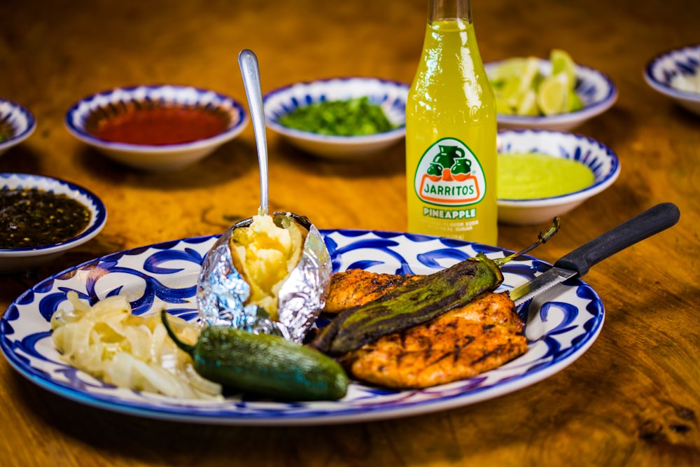 green glass bottle beside white and blue ceramic plate with food