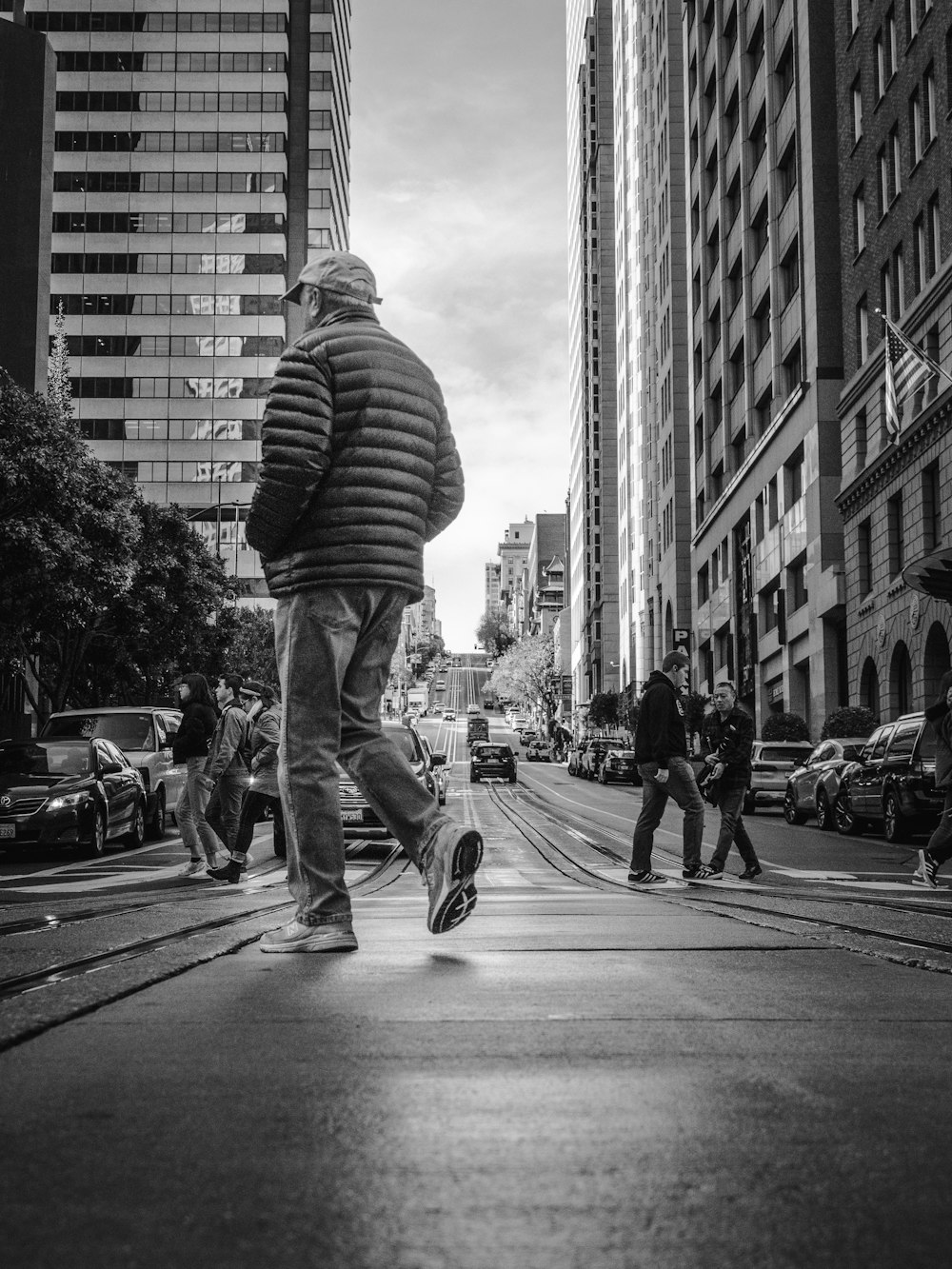 grayscale photo of man in striped shirt and denim jeans walking on street