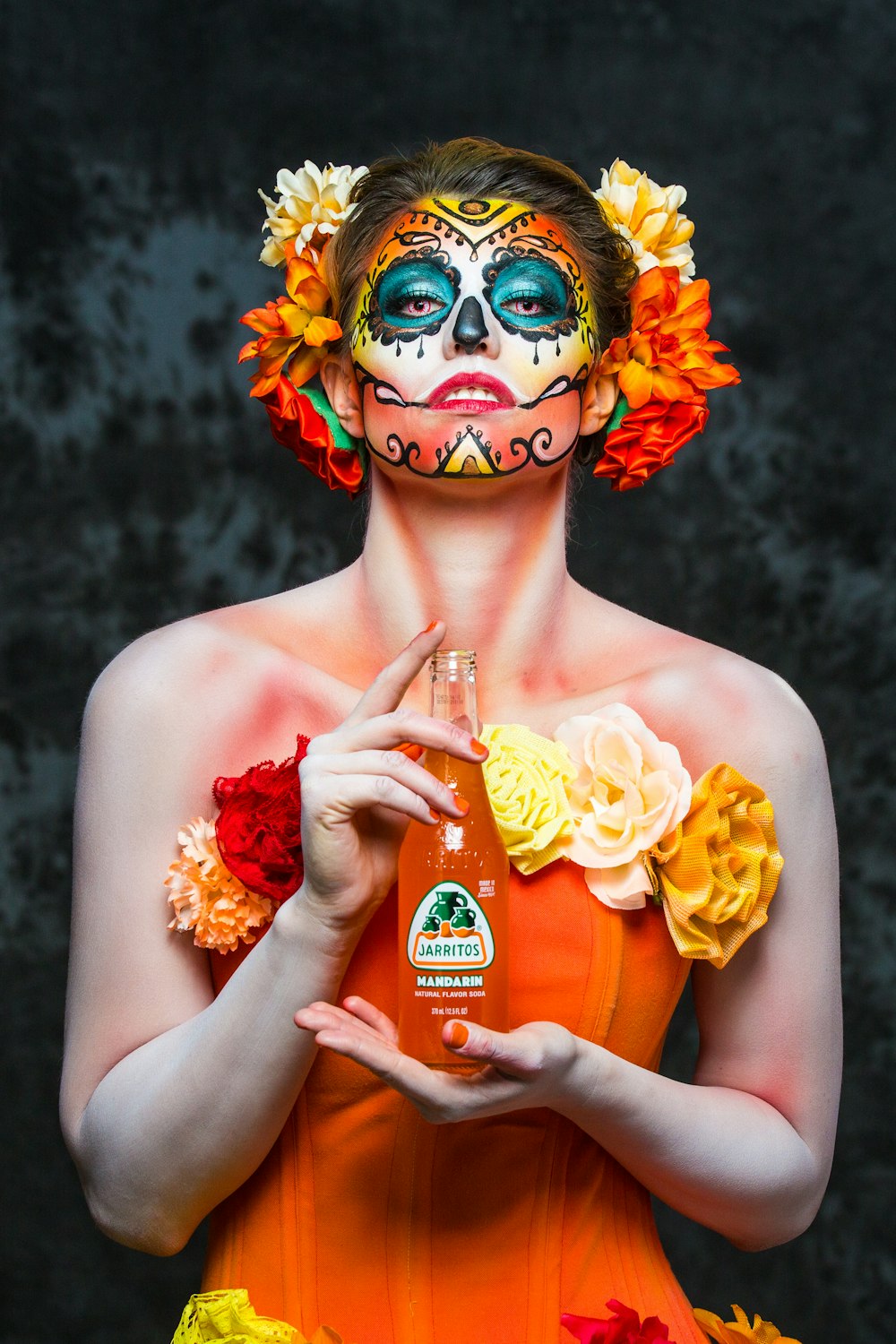 woman with yellow and red floral headdress holding bottle with red liquid