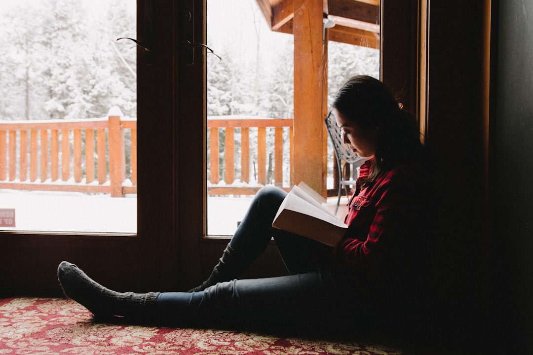 woman in red and white long sleeve shirt and black pants sitting on floor, Woman reading her Bible in a snowy cabin