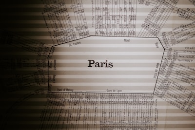 A vintage train schedule centered around the name Paris, with various station names and times laid out in a radial pattern. The text is printed in a dark, classic font on a beige, slightly translucent background that has subtle horizontal lines.