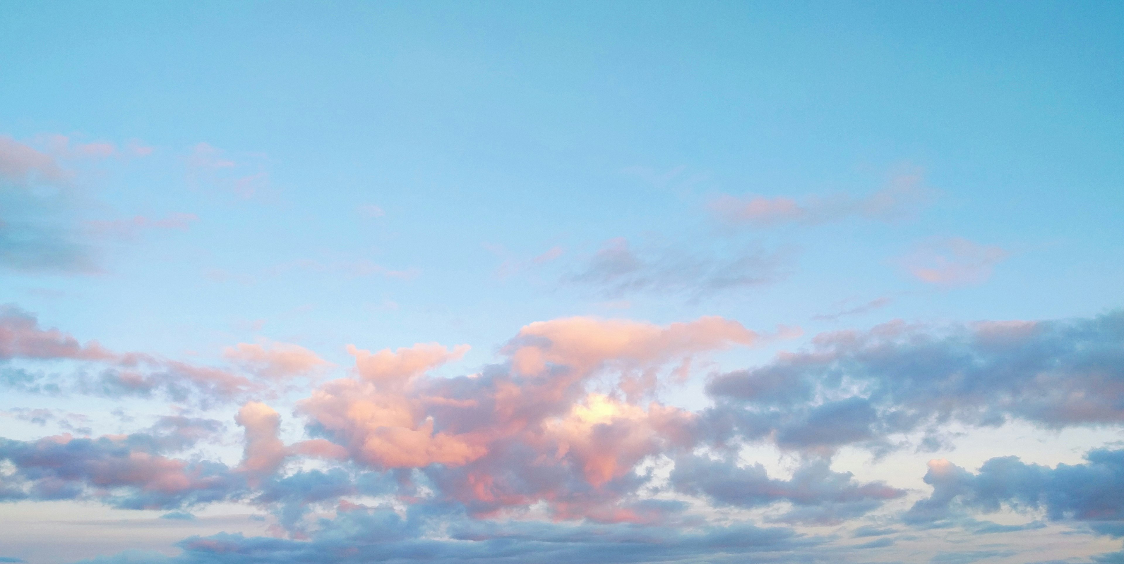 Pink, blue, and yellow clouds against a clear, blue sky at sunset. 