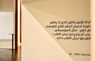 A wall with a geometric design displaying Arabic text in black font. The setting appears to have a minimalistic and modern aesthetic with warm lighting.