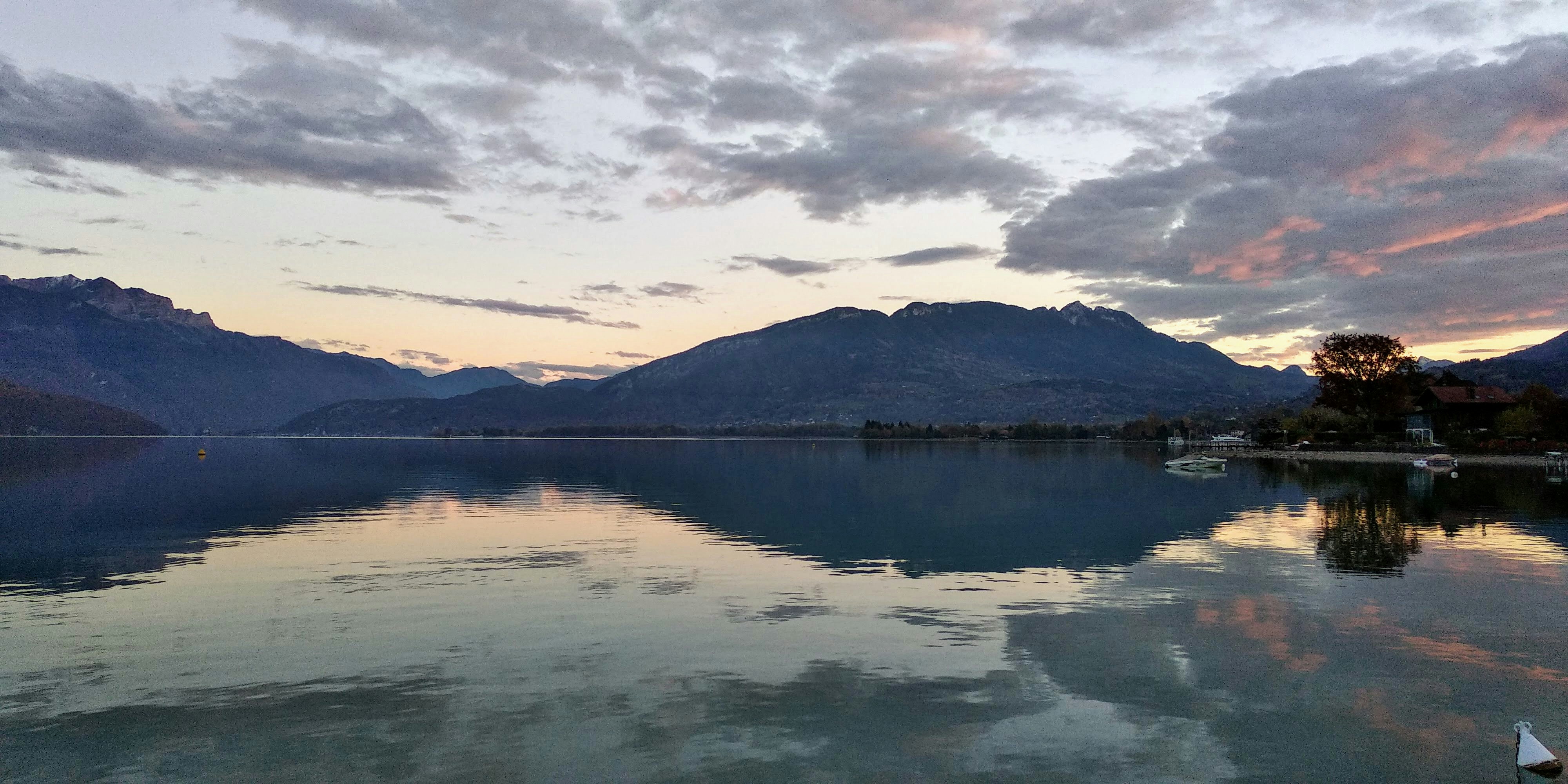 Serene mountain lake at dusk, dark reflective water, dim atmospheric lighting, deep shadows at shoreline