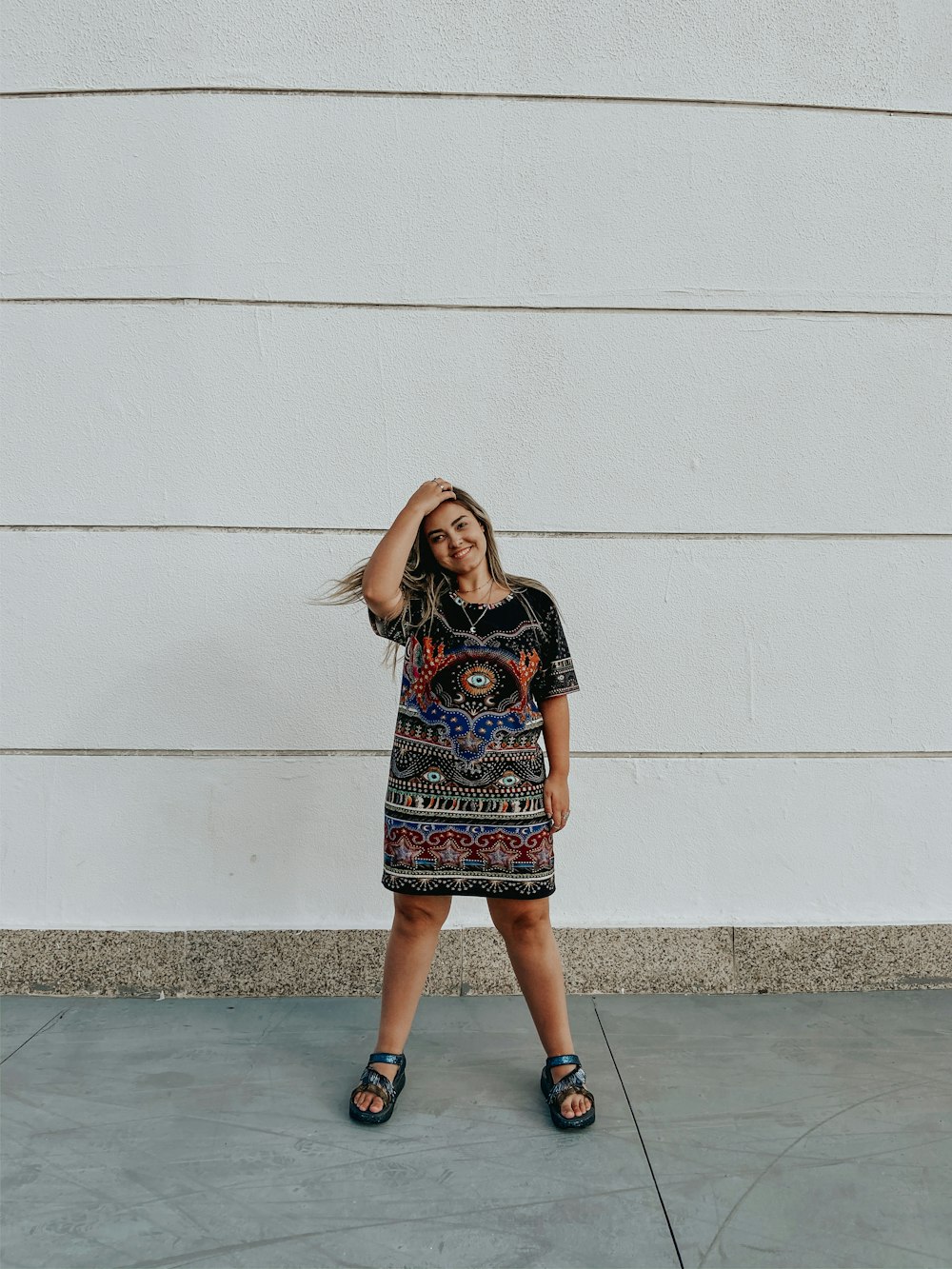 woman in black and red floral dress standing beside white wall