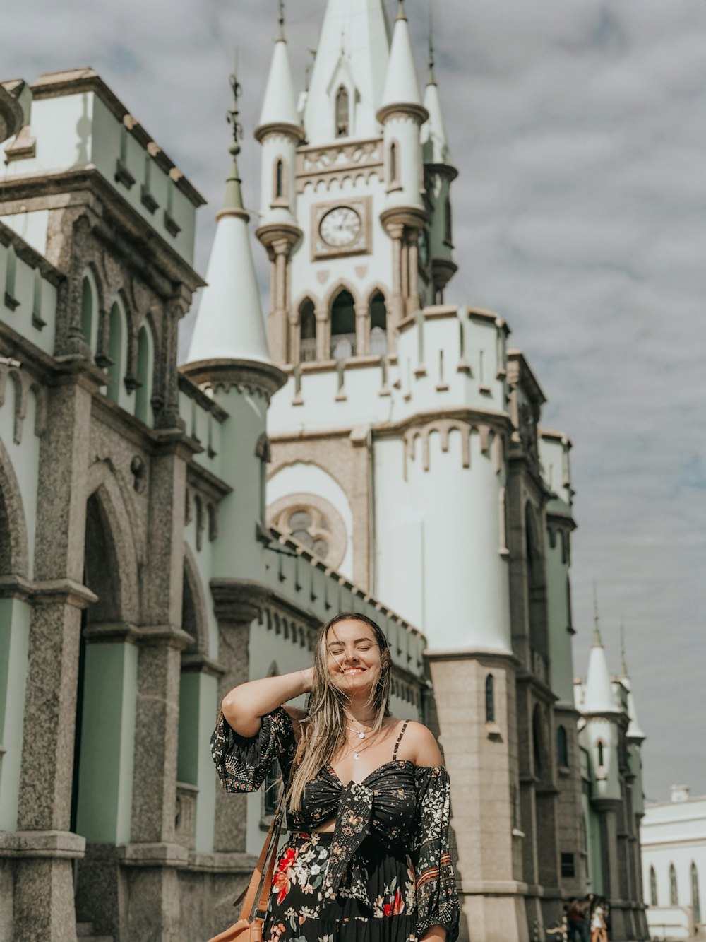 smiling woman in black and white floral sleeveless dress standing near white concrete building during daytime