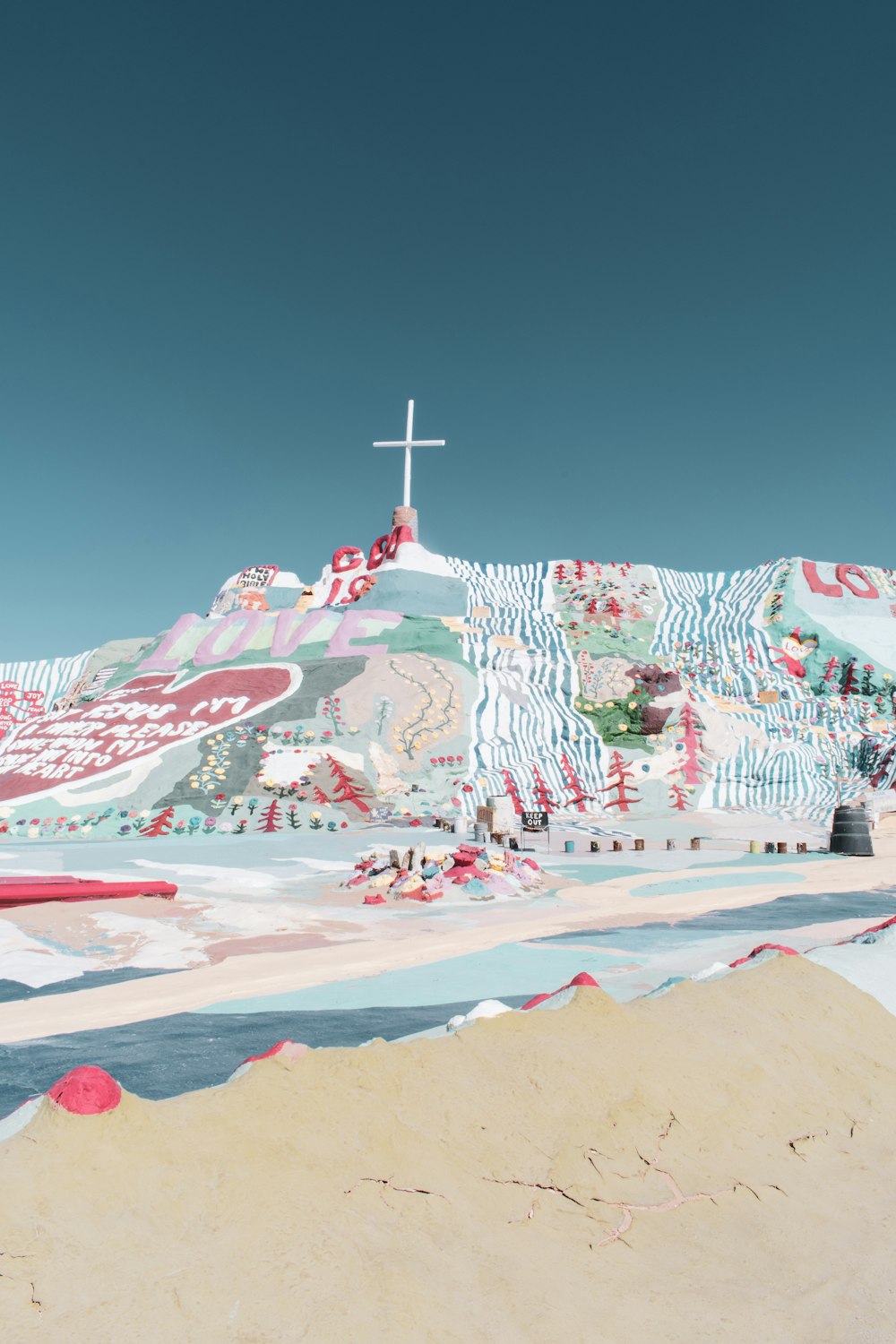 white and red concrete cross on white sand under blue sky during daytime