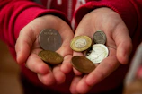 A hand holding a small collection of diverse coins from different countries.