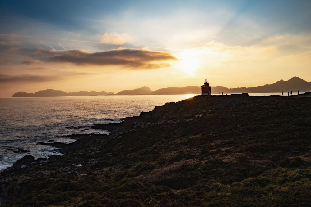 silhouette of lighthouse near body of water during sunset