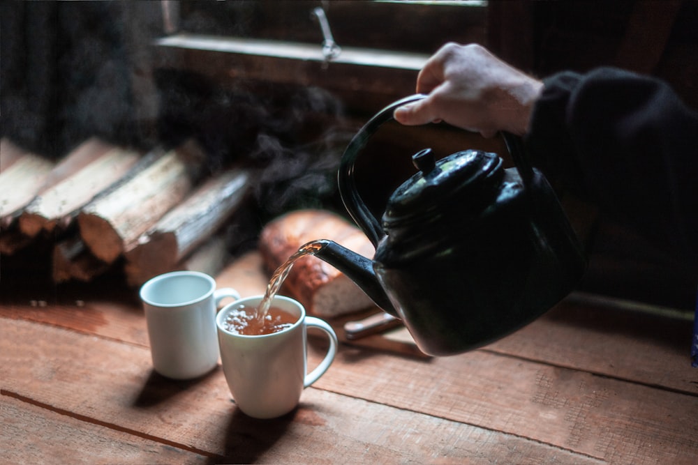 person pouring tea on white ceramic mug