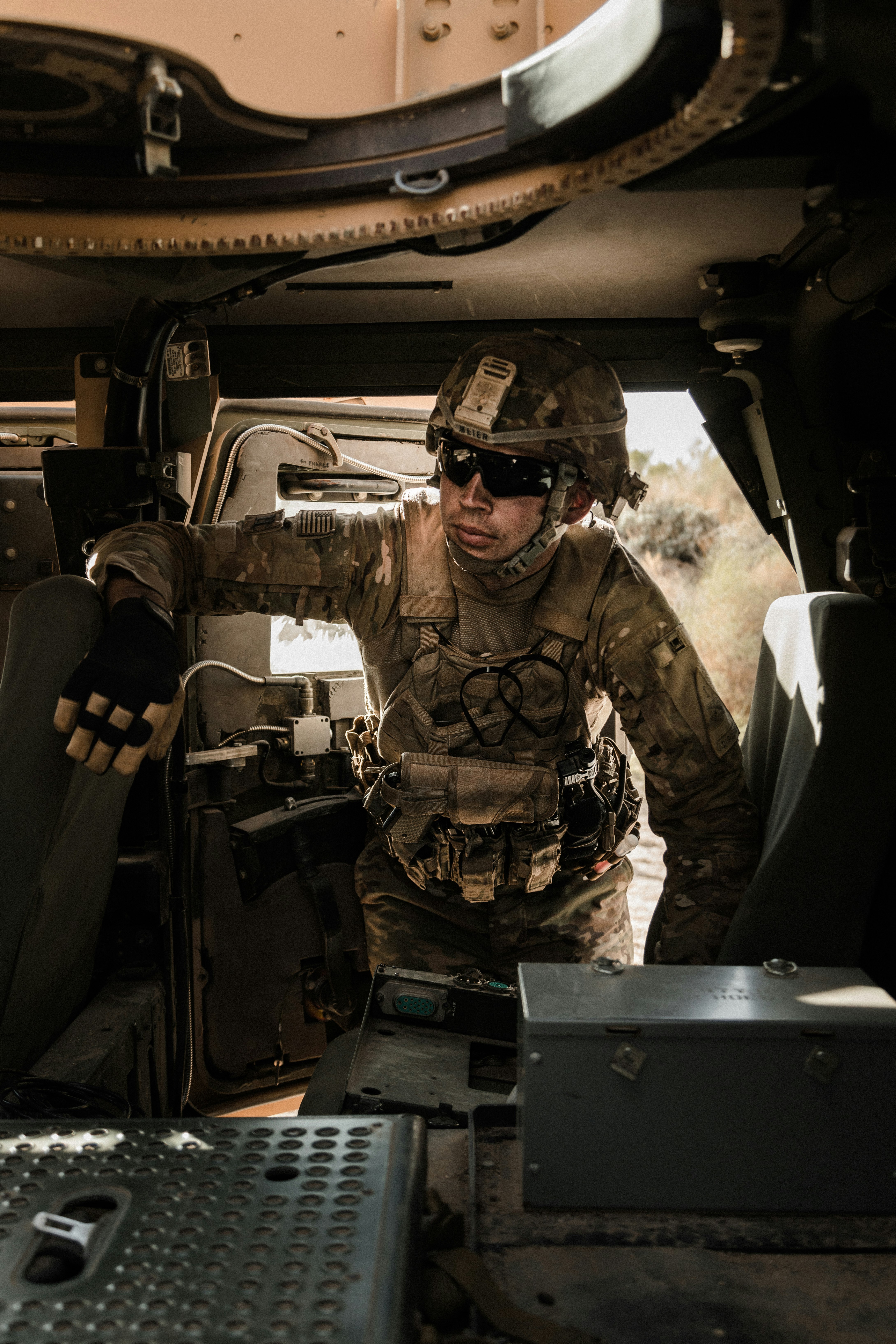 man in brown and black camouflage uniform sitting on black car seat during daytime