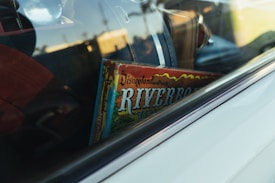 A vintage game box labeled 'Disneyland Riverboat' is visible through the window of a car, surrounded by various travel bags.