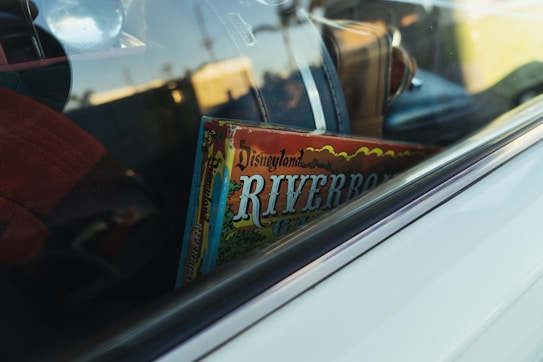 A vintage game box labeled 'Disneyland Riverboat' is visible through the window of a car, surrounded by various travel bags.