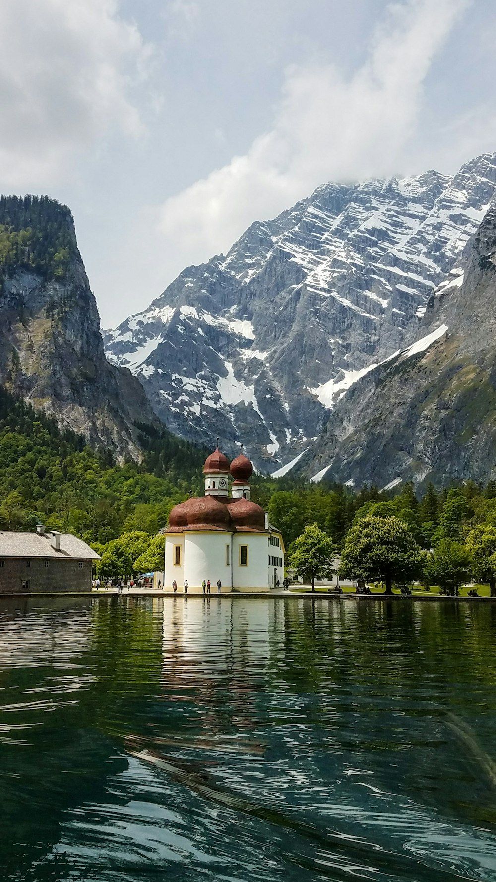 white and red concrete building near body of water and green trees and mountain during daytime