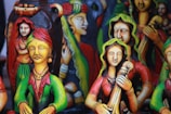 Colorful clay figurines depicting traditional musicians and dancers, adorned with vibrant attire, intricate jewelry, and expressive facial details. The sculptures have a folk art style with vivid use of color, creating a lively and cultural atmosphere.