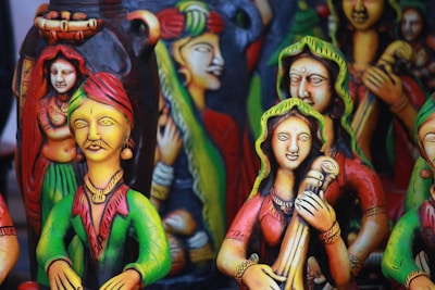 Colorful clay figurines depicting traditional musicians and dancers, adorned with vibrant attire, intricate jewelry, and expressive facial details. The sculptures have a folk art style with vivid use of color, creating a lively and cultural atmosphere.