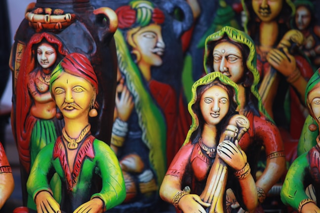 Colorful clay figurines depicting traditional musicians and dancers, adorned with vibrant attire, intricate jewelry, and expressive facial details. The sculptures have a folk art style with vivid use of color, creating a lively and cultural atmosphere.