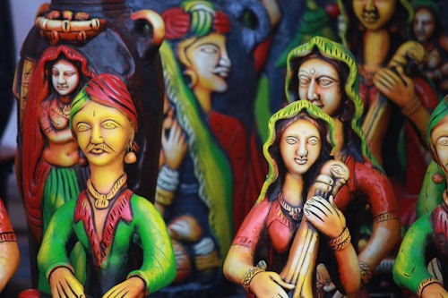 Colorful clay figurines depicting traditional musicians and dancers, adorned with vibrant attire, intricate jewelry, and expressive facial details. The sculptures have a folk art style with vivid use of color, creating a lively and cultural atmosphere.