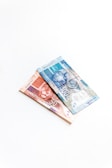 Two banknotes, one valued at 100 and the other at 50, featuring images of animals, are placed on a white surface. The notes are intricately designed with vibrant colors and details.