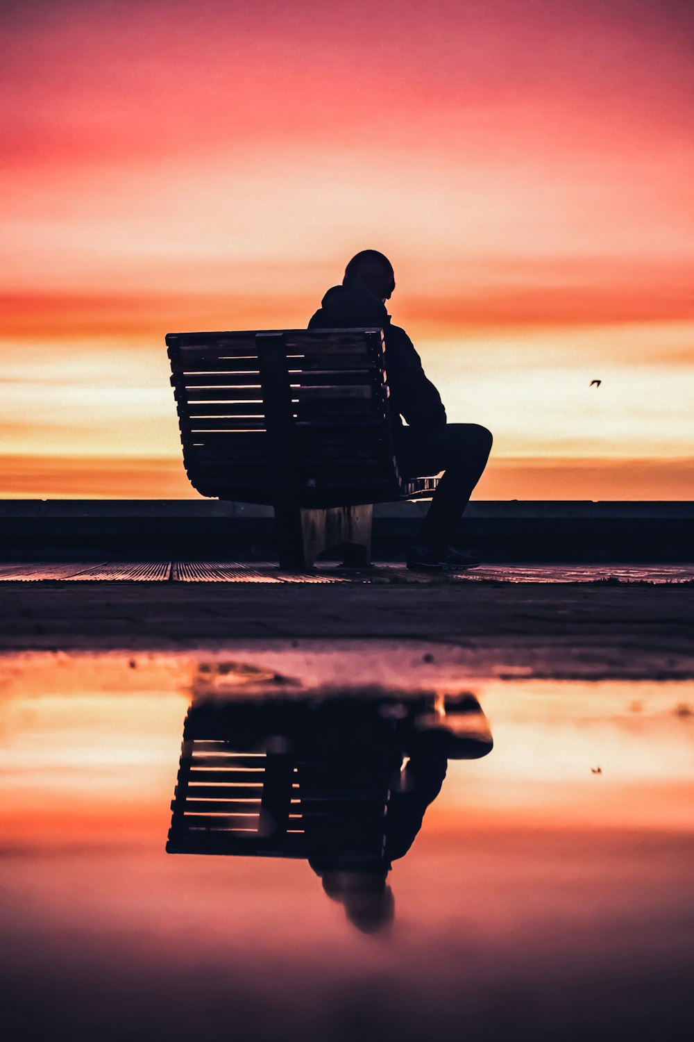 Silhouette eines Mannes, der während des Sonnenuntergangs auf einer Bank in der Nähe des Strandes sitzt