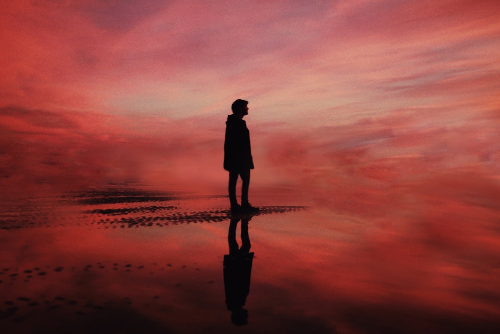 silhouette of man standing on beach during sunset