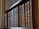 A row of antique, leather-bound books with ornate spines are neatly arranged on a wooden bookshelf.