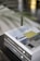 A close-up of two stacked hardcover books with the title 'Buitengewoon & Betaalbaar Bouwen' visible on the spines. The cover displays an image of a modern architectural design featuring a house with a large window and yellow accent panel. The background includes blurred elements, possibly consisting of plant leaves, adding a touch of natural ambiance.