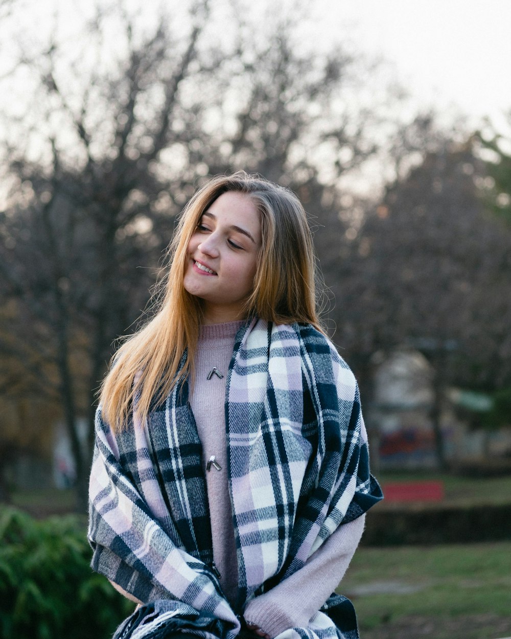 woman in white and blue plaid button up shirt standing near trees during daytime