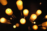 Softly lit arrangement of white candles surrounded by small golden stars and astral symbols on a dark blue background.