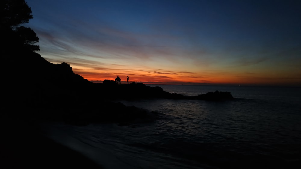 silhouette of mountain near body of water during sunset