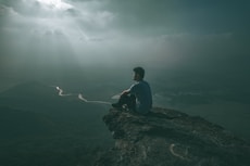 man in blue shirt sitting on rock formation during daytime