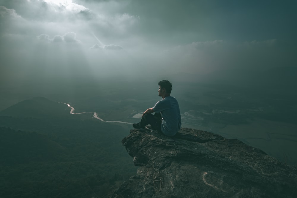 man in blue shirt sitting on rock formation during daytime