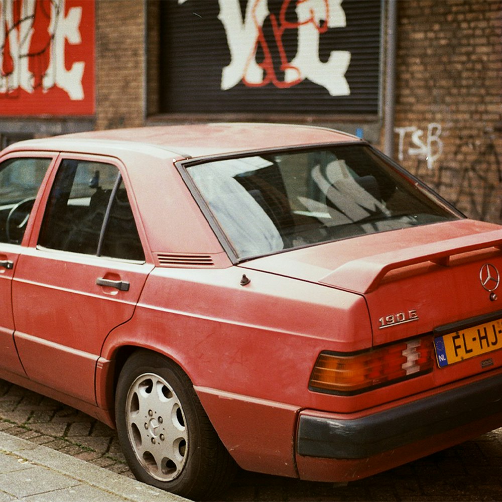 pink sedan parked beside red and white building during daytime