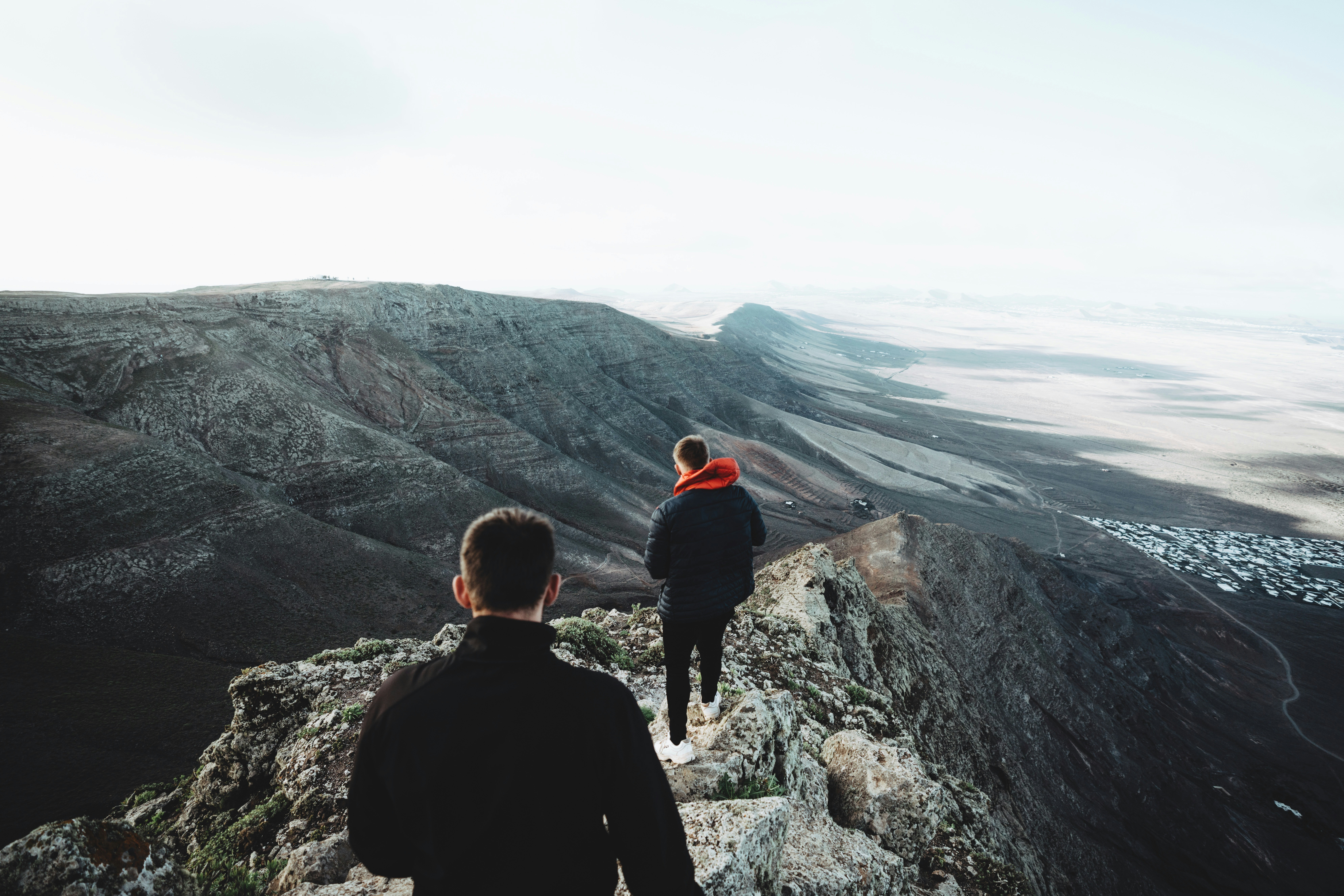 man in black jacket sitting on rock looking at the mountains during daytime