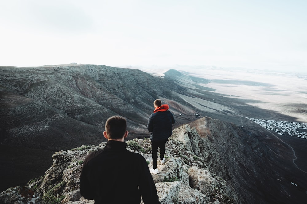 man in black jacket sitting on rock looking at the mountains during daytime