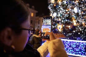 person holding iphone taking photo of lighted christmas tree