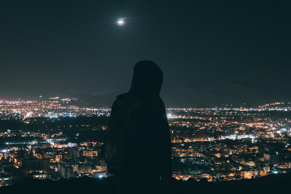 silhouette di persona in piedi sulla cima dell'edificio durante la notte