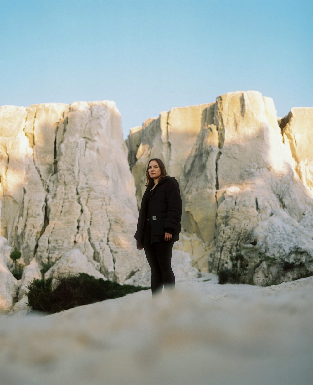 donna in cappotto nero in piedi su terreno coperto di neve bianca durante il giorno