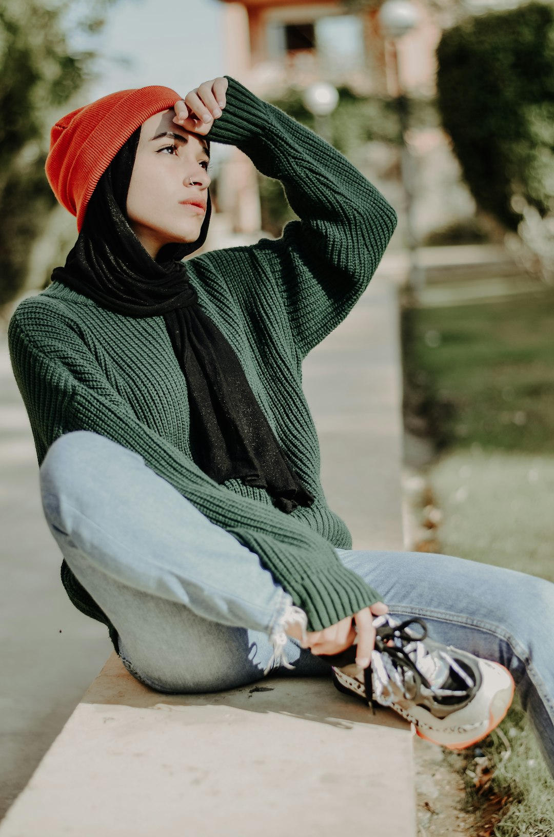 woman in green and black hijab and blue denim jeans sitting on concrete bench during daytime