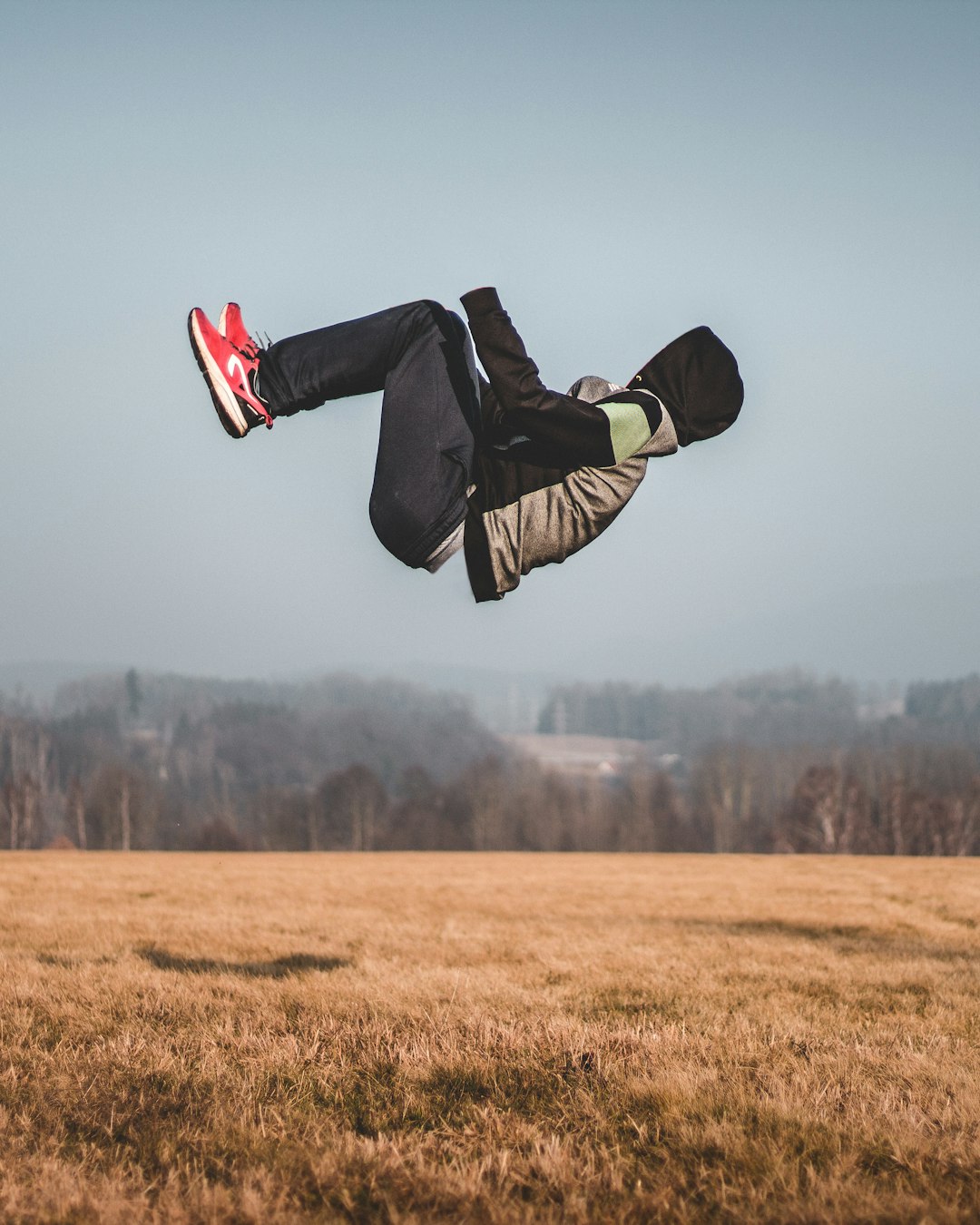 person in black jacket and red and white sneakers jumping on air