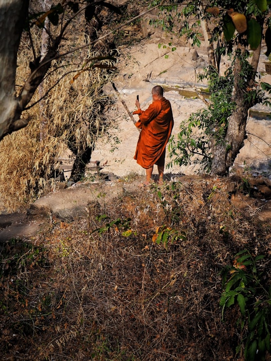 man in orange robe walking on gray rocky road during daytime in Khon Phapheng Falls Laos