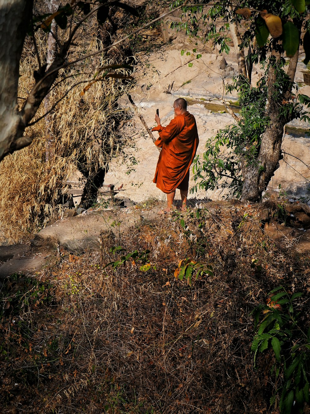 man in orange robe walking on gray rocky road during daytime