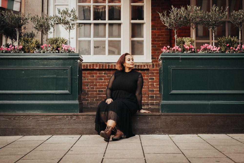donna in camicia nera a maniche lunghe seduta sul marciapiede durante il giorno