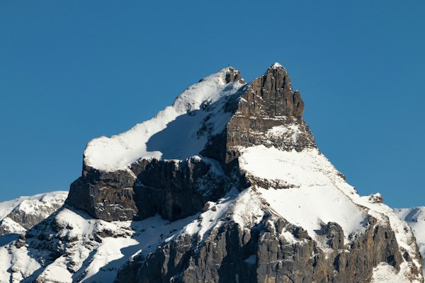 A twin-summit rock peak plastered with snow under a deep blue winter sky in the Uri Alps above Engelberg