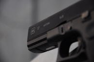 A close-up view of a black handgun, with visible engravings including the brand and model details. The focus is on the slide of the firearm.