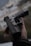A hand is holding a black handgun against a blurred, neutral background. The focus is on the firearm, highlighting its details and structure.
