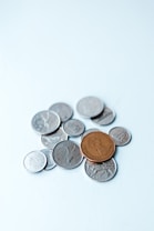 A collection of assorted coins with one larger brown coin placed prominently on top of several smaller silver coins on a light blue surface.